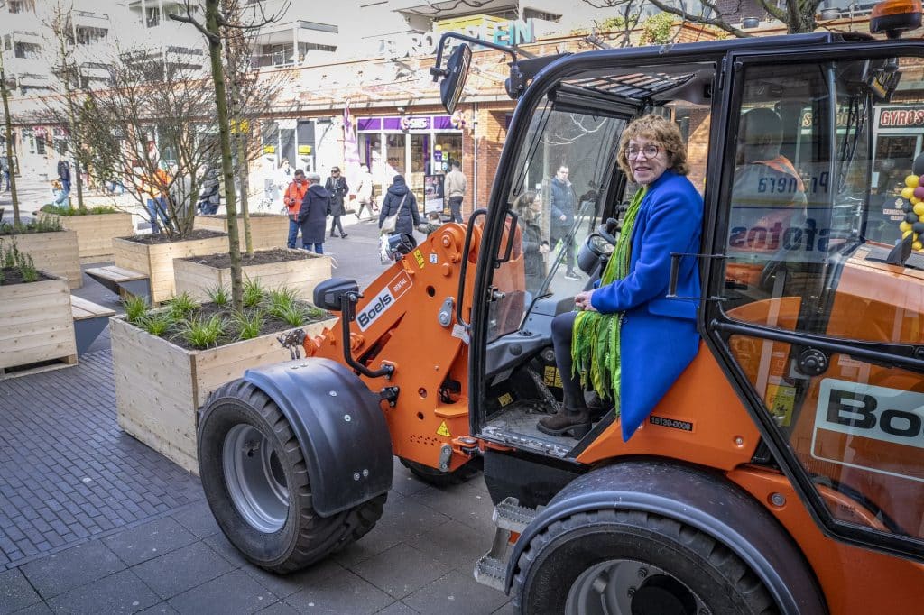Wethouder Anjo van de Ven verplaatst een houten bak met planten en een boom voor het Wandelend Bos.