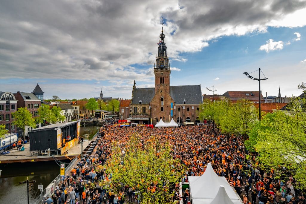 Grote menigte in oranje op het Waagplein in Alkmaar tijdens Koningsdag, met de Waagtoren op de achtergrond.