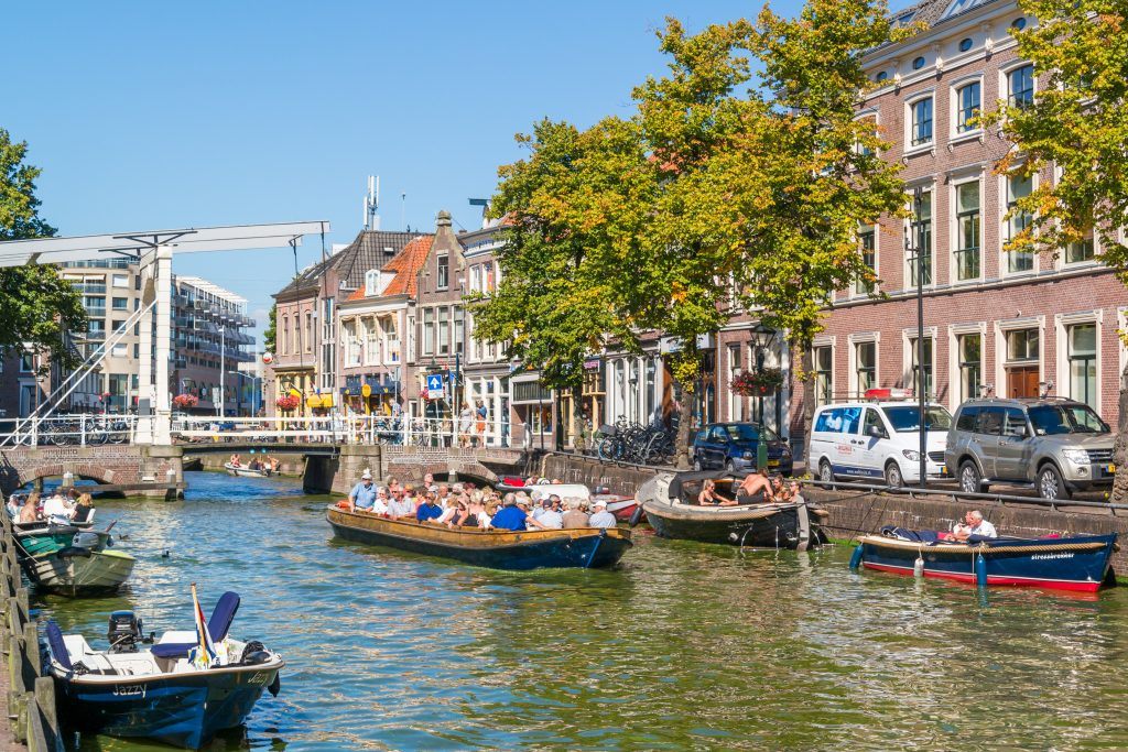 Meerdere boten varen door een drukke gracht in Alkmaar met mensen langs de kade en op het water.