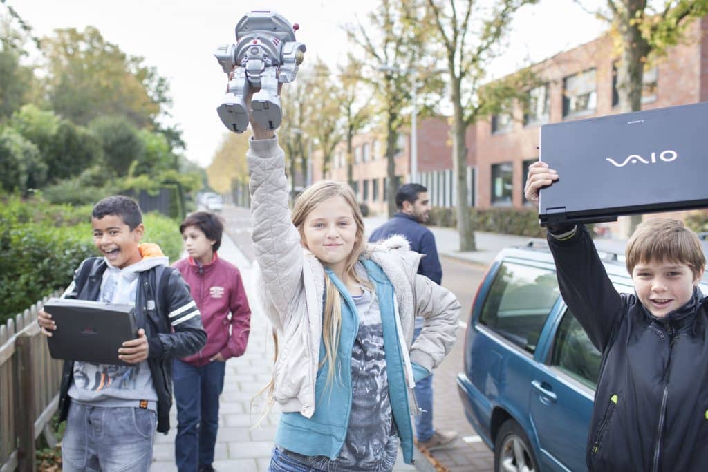 4 kinderen in een woonwijk houden opgehaalde elektrische apparaten omhoog.