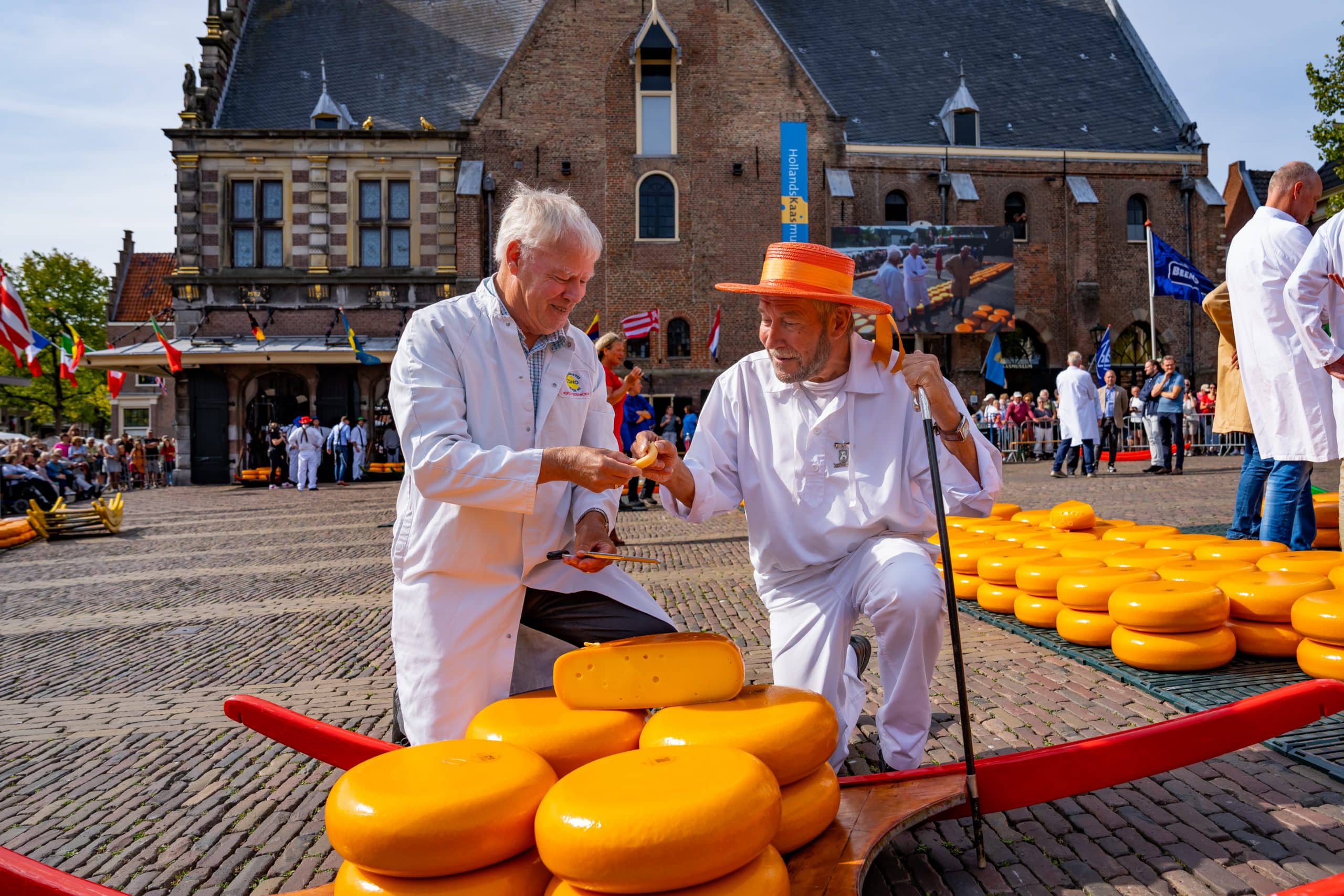 twee kaasdragers delen een stukje kaas op de kaasmarkt op het Waagplein in Alkmaar
