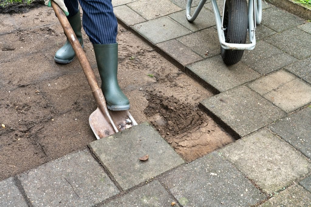 Met een schep haalt iemand tegels uit de tuin