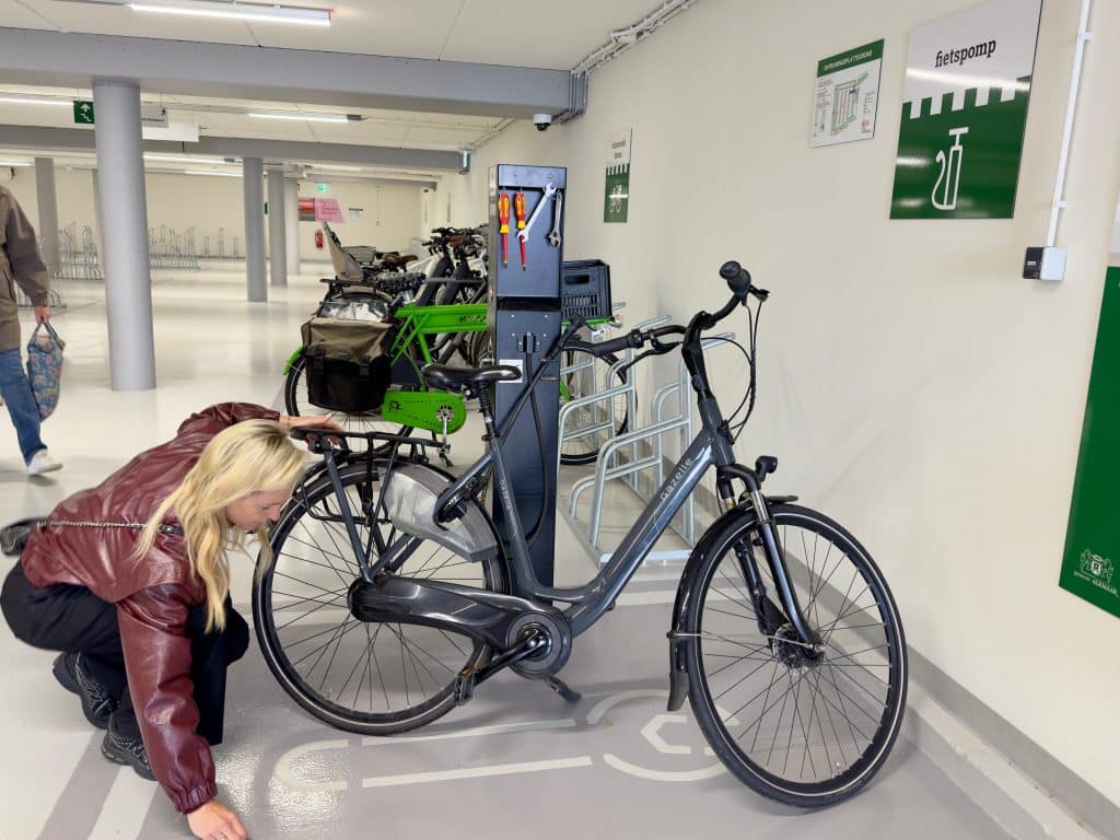 mevrouw pompt haar banden op bij de fietsenpomp in de fietsenstalling.