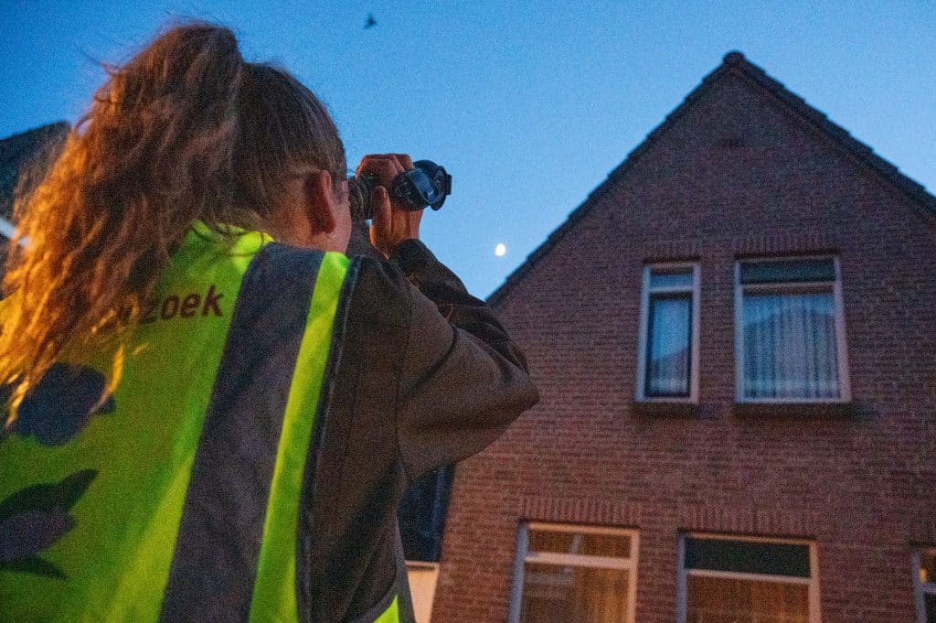 Onderzoeker in geel hes kijkt met infraroodcamera naar een gevel van een woning in Alkmaar.