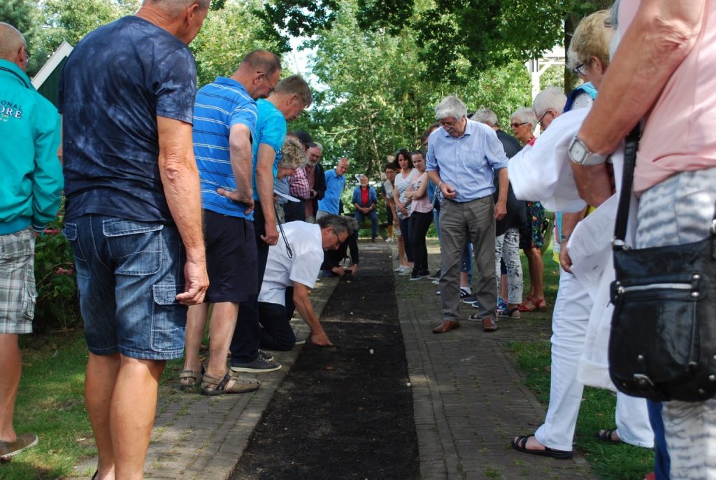 Mensen kijken naar een knikkerwedstrijd op een knikkerbaan in Grootschermer.
