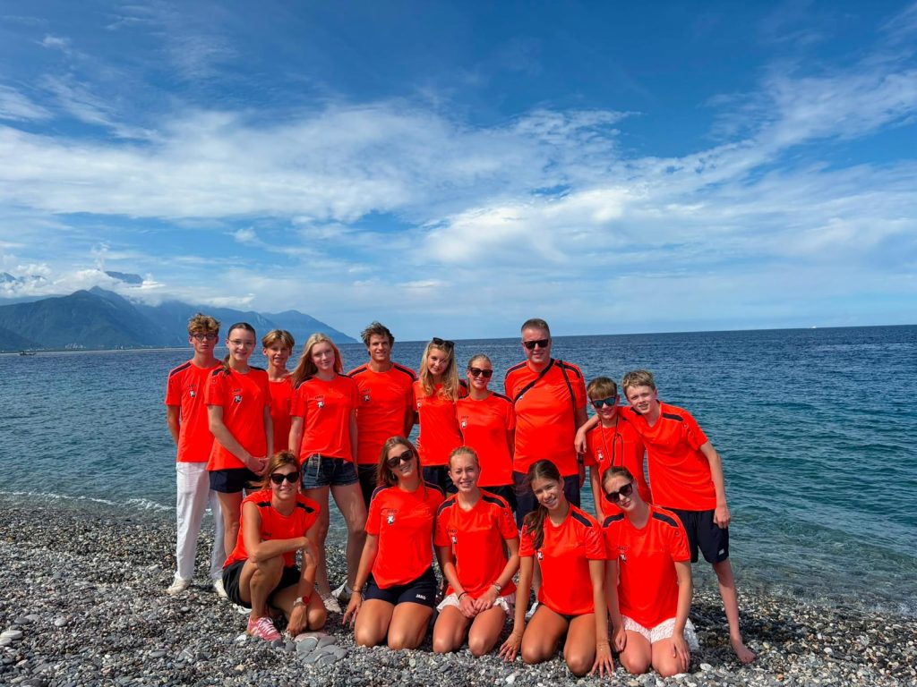 Sporters en begeleiders van Team Alkmaar poseren samen aan de kust in Taiwan.