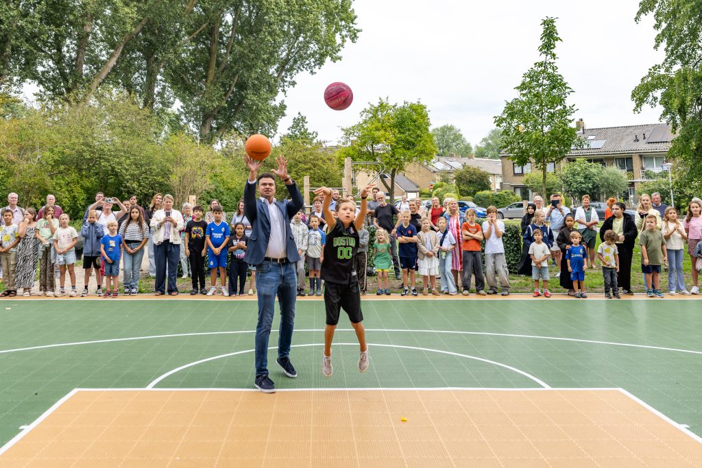 Wethouder en leerling gooien een basketbal op de vernieuwde sport- en beweegplek aan de Blanckerhofweg.