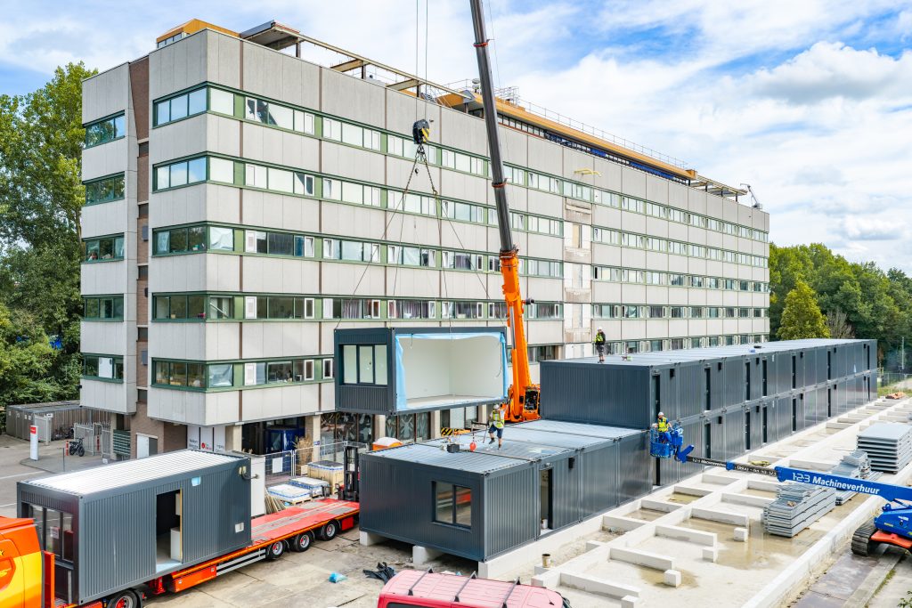 Een hijskraan plaatst een tijdelijke woning tussen de andere woonunits aan de Robonsbosweg.
