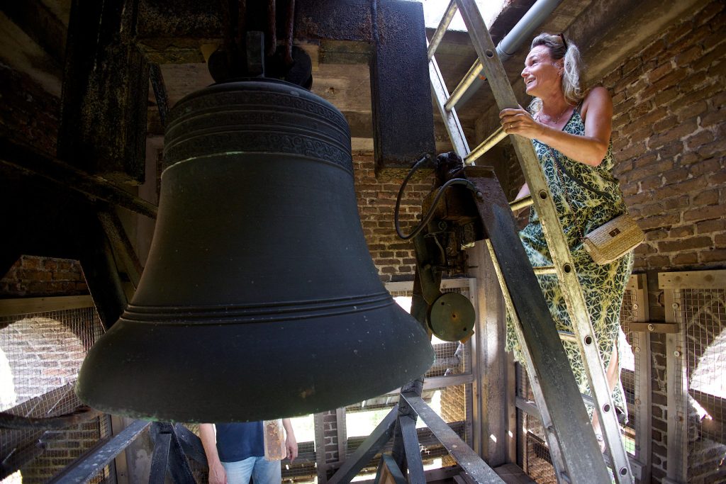 Bezoeker beklimt de toren van de kerk in Stompetoren, naast een grote kerkklok.