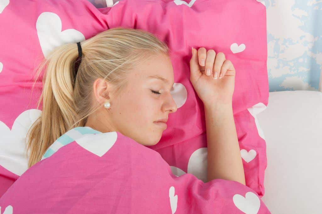 tiener slaapt in bed onder een roze dekbedovertrek met hartjes