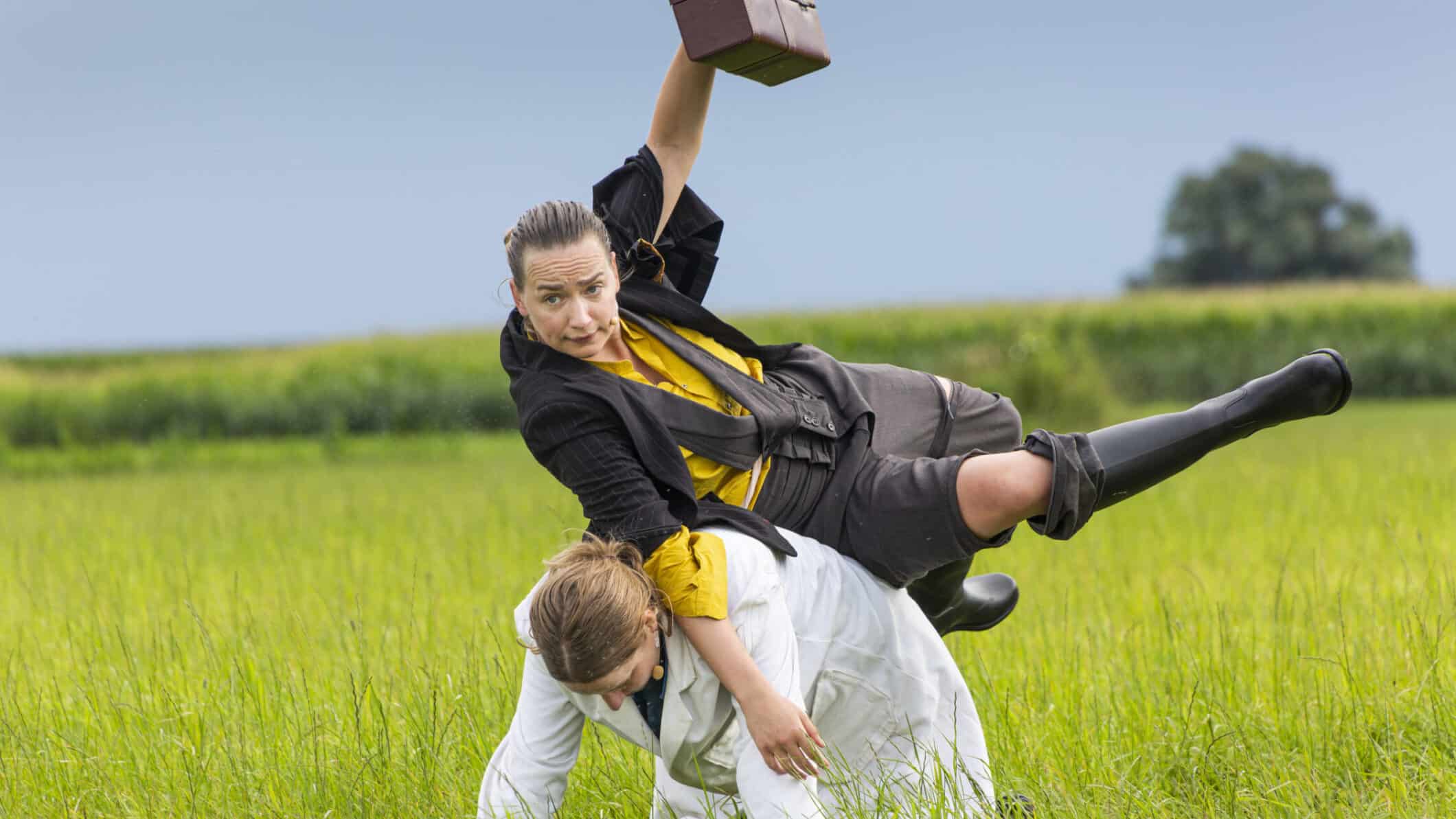 een vrouw zit gehurkt in een grasveld en een andere valt sierlijk over haar heen