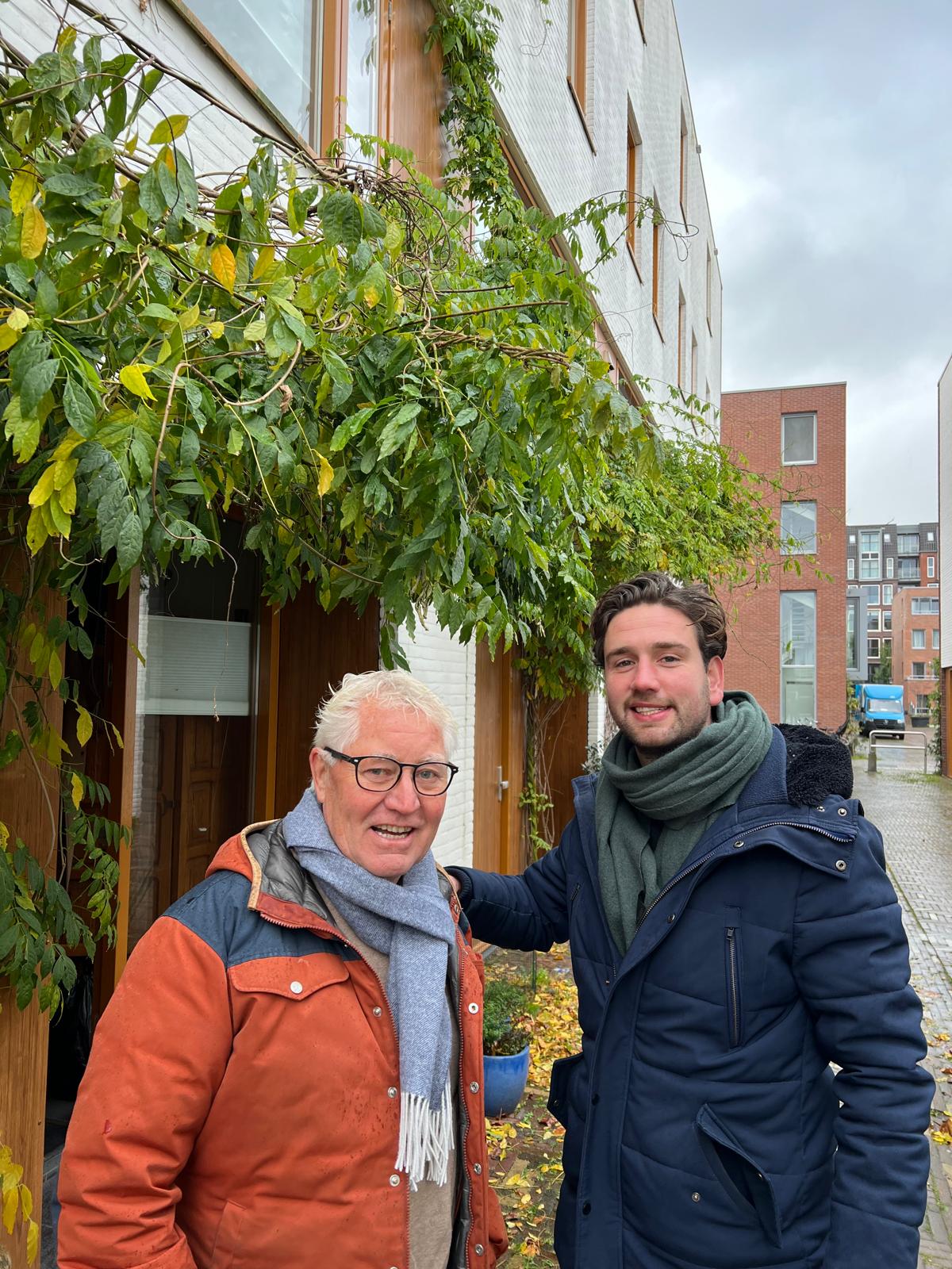 Een jonge man en een oudere man staan voor een gebouw met veel planten op de gevel