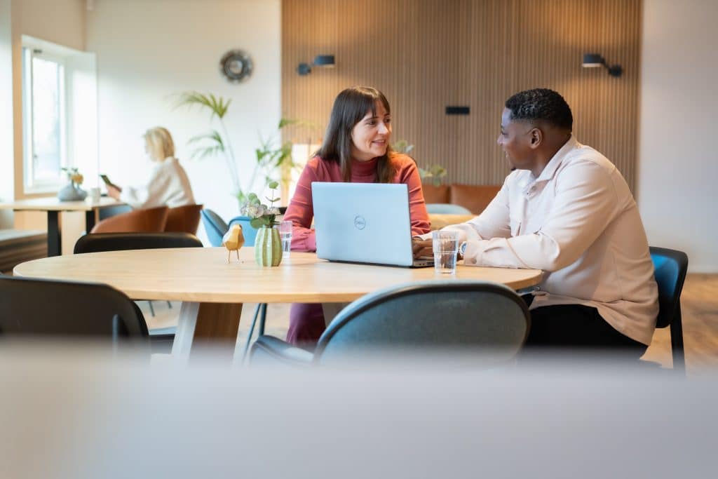 Man en vrouw zitten aan tafel met een laptop voor hen, ze overleggen met elkaar.