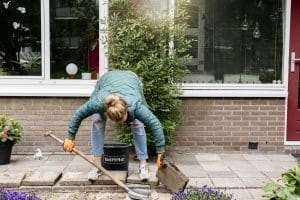 Vrouw staat gebukt met een schep en haalt tegels uit de straat