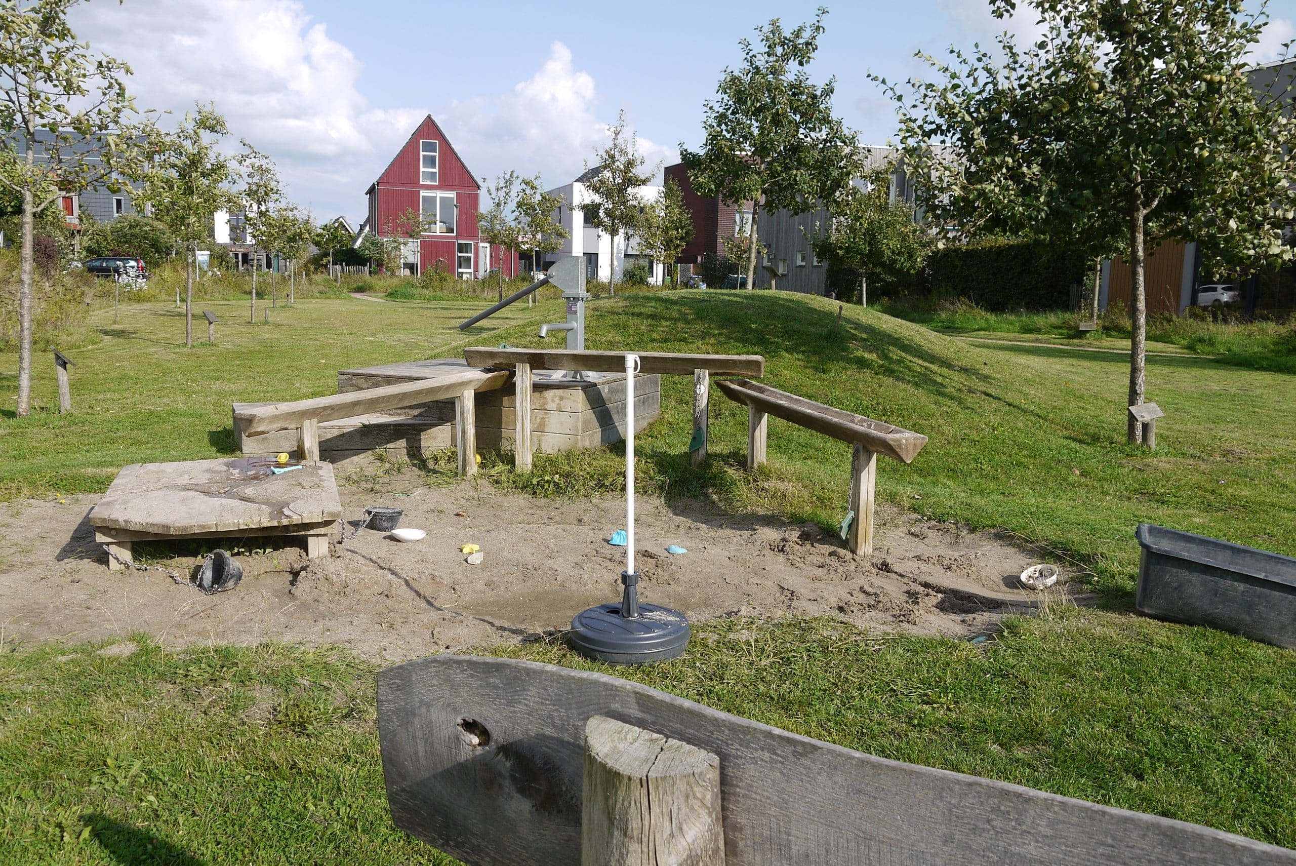 Speeltuin met een houten waterpomp en waterbaan met gras eromheen.