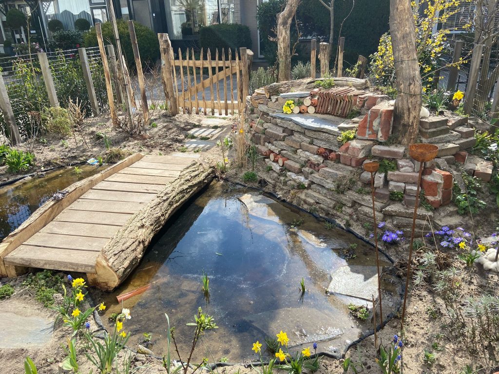 Regenwatervijver in een voortuin met een stapelmuur en een bruggetje erover.