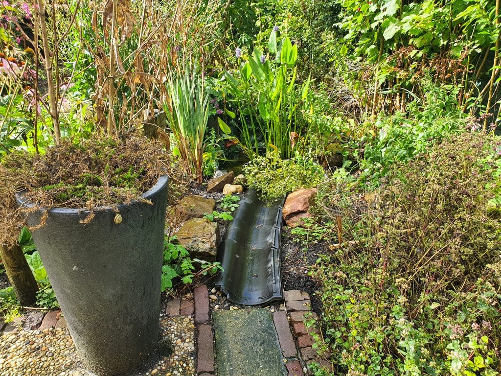 Een klein goot van dakpannen en stenen die naar een regenwatervijver loopt.