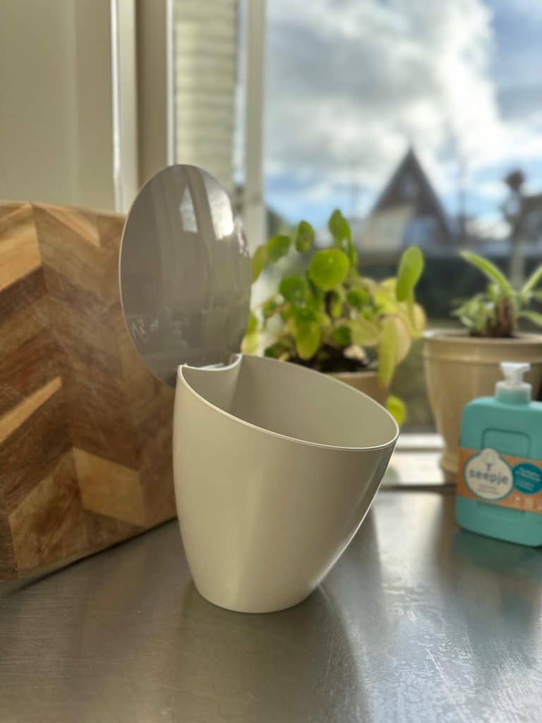 gft-keukenbakje op een aanrecht met op de achtergrond een snijplank, plantje en handzeeppompje