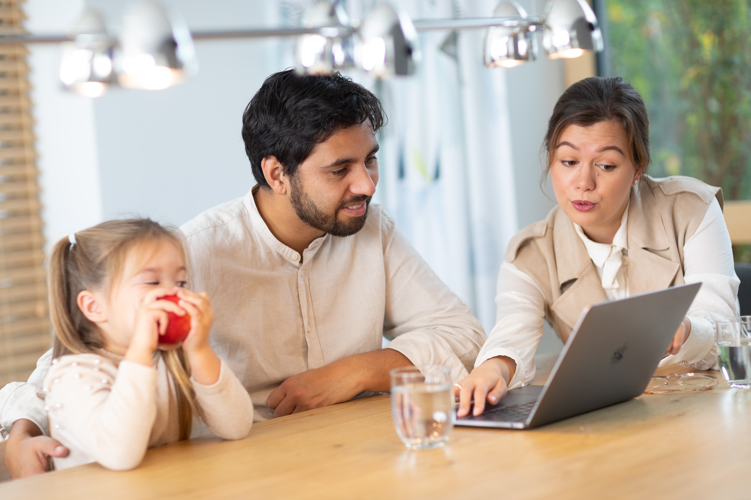 Een vrouw geeft bij een laptop uitleg aan een man. Er is ook een kind bij aanwezig.