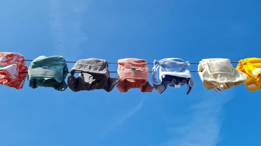 Gekleurde wasbare luiers aan een waslijn buiten met op de achtergrond blauwe lucht.